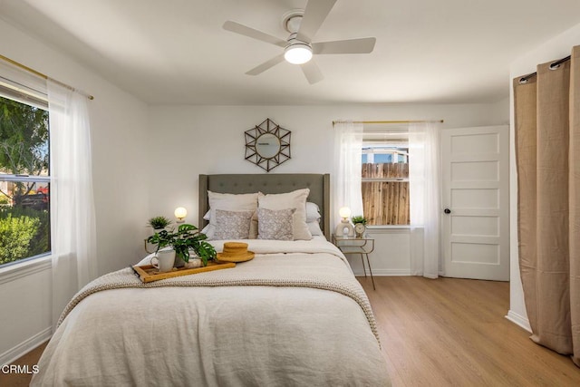 bedroom featuring a ceiling fan, baseboards, multiple windows, and wood finished floors