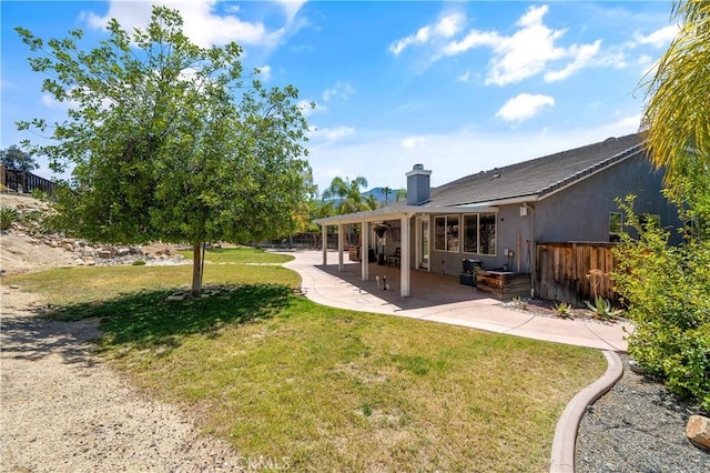 rear view of property featuring fence, stucco siding, a chimney, a patio area, and a lawn