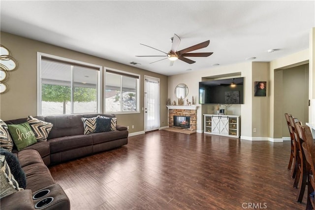 living area with a ceiling fan, a stone fireplace, visible vents, wood finished floors, and baseboards