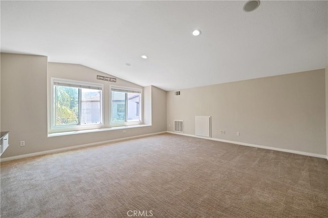 carpeted empty room with baseboards, vaulted ceiling, and visible vents
