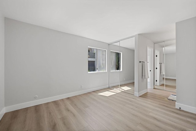 unfurnished bedroom featuring light wood-style floors, baseboards, and multiple closets