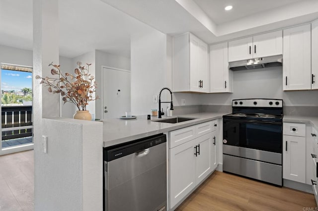 kitchen with a peninsula, under cabinet range hood, white cabinets, a sink, and stainless steel appliances