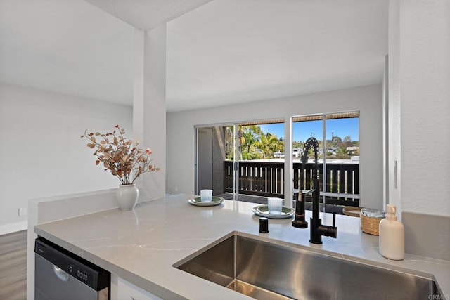kitchen with stainless steel dishwasher, wood finished floors, a sink, and light countertops