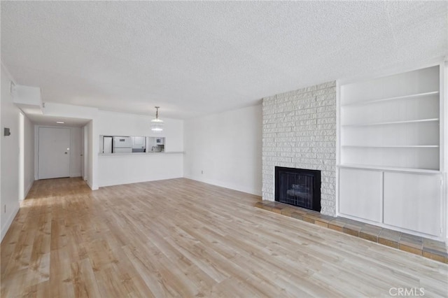 10966 Rochester Ave Unit 5D, Los Angeles, CA 90024 - unfurnished living room featuring a textured ceiling, wood finished floors, a brick fireplace, and built in shelves