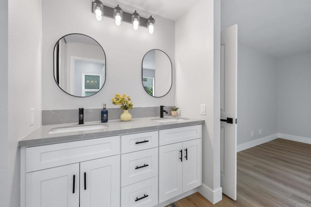 full bath featuring double vanity, baseboards, a sink, and wood finished floors