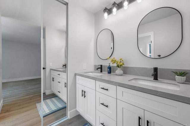 full bath with a sink, baseboards, double vanity, and wood finished floors