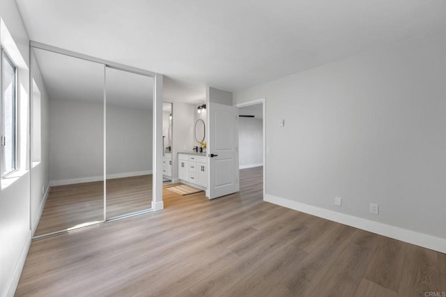unfurnished bedroom with a closet, baseboards, light wood finished floors, and ensuite bath