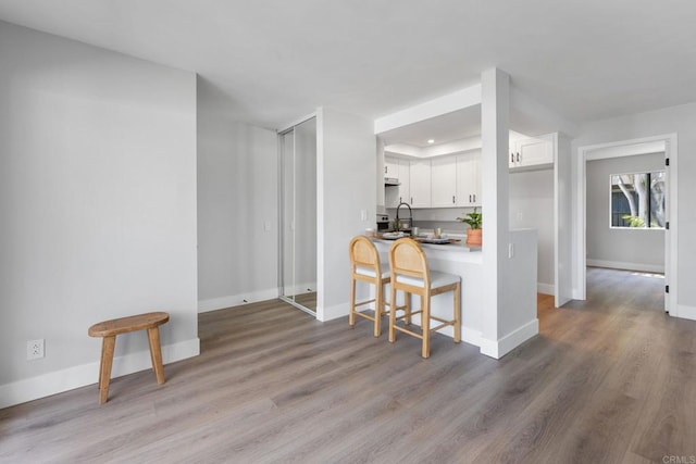 kitchen with a peninsula, wood finished floors, baseboards, a kitchen breakfast bar, and white cabinetry