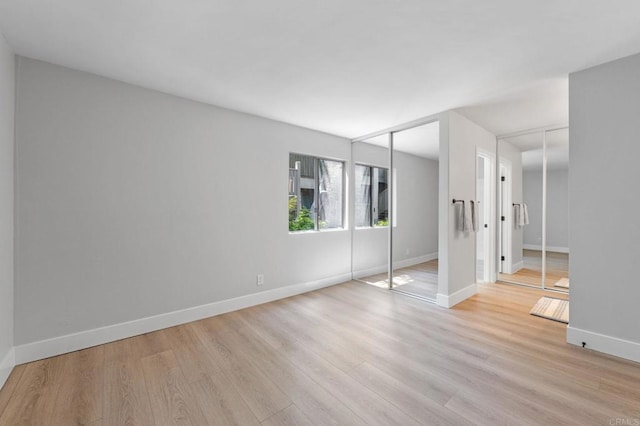 unfurnished bedroom featuring two closets, baseboards, and light wood finished floors
