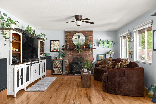 living area featuring ceiling fan, a wood stove, wood finished floors, and visible vents