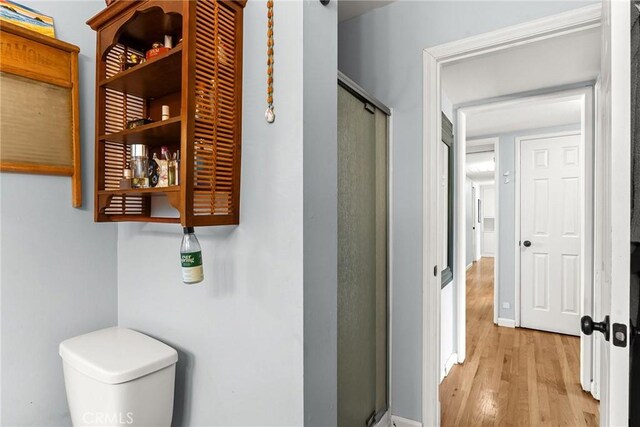 full bathroom with baseboards, wood finished floors, toilet, and a shower stall