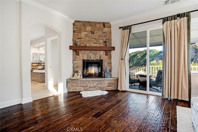 living area featuring crown molding, arched walkways, a stone fireplace, and hardwood / wood-style floors