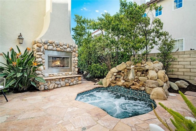 view of swimming pool featuring an outdoor stone fireplace, an in ground hot tub, fence, and a patio