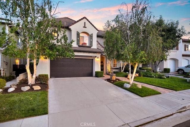 mediterranean / spanish house featuring an attached garage, a tile roof, stucco siding, a front yard, and concrete driveway