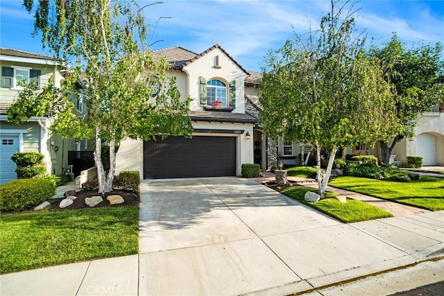 mediterranean / spanish house featuring an attached garage, a tile roof, stucco siding, a front yard, and driveway