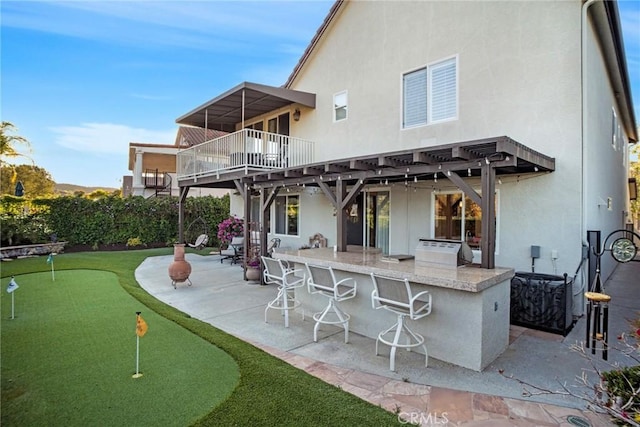 back of property with a balcony, a patio, stucco siding, area for grilling, and outdoor wet bar