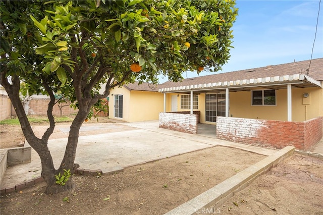back of property with fence, roof with shingles, stone siding, stucco siding, and a patio