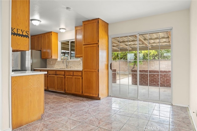 kitchen with brown cabinets, a sink, light countertops, freestanding refrigerator, and tasteful backsplash