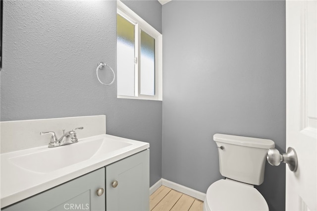 half bath with toilet, baseboards, wood finished floors, and vanity