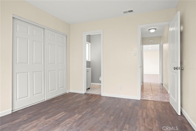 unfurnished bedroom with visible vents, dark wood finished floors, baseboards, and a closet
