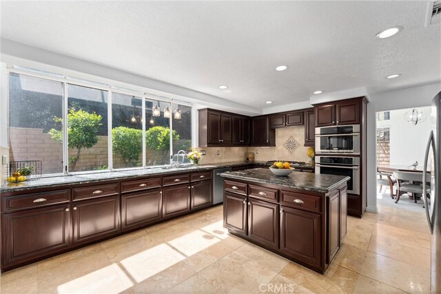 1720 San Alvarado Cir, Corona, CA 92882 - kitchen with appliances with stainless steel finishes, a sink, tasteful backsplash, dark brown cabinets, and a kitchen island