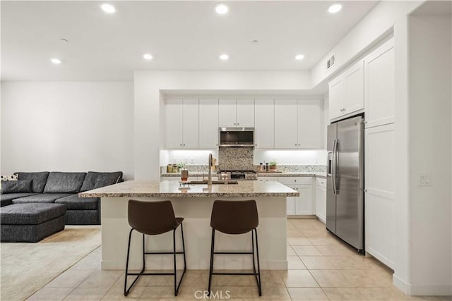 kitchen with light stone counters, a sink, light tile patterned floors, and stainless steel appliances