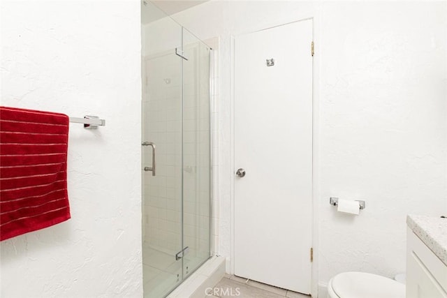 bathroom with tile patterned flooring, a stall shower, vanity, toilet, and a textured wall