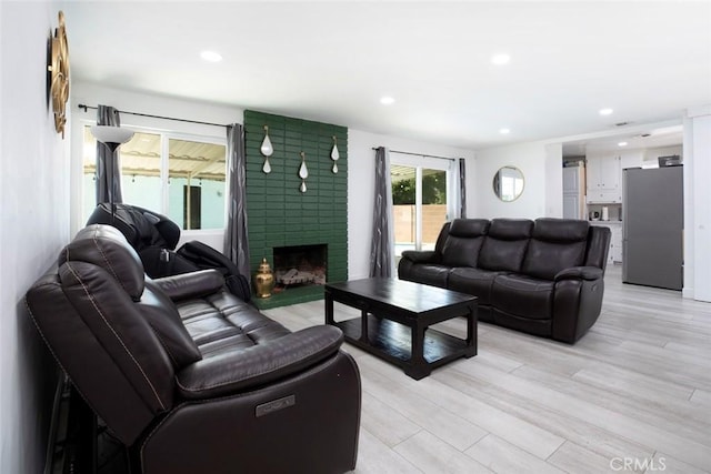 living room with a brick fireplace, recessed lighting, and light wood finished floors