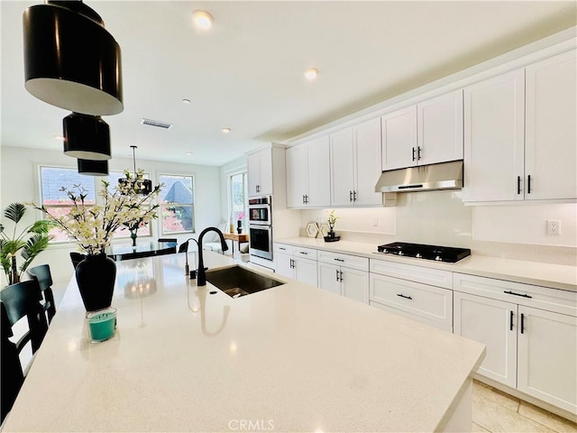 kitchen featuring a sink, double oven, light countertops, under cabinet range hood, and visible vents