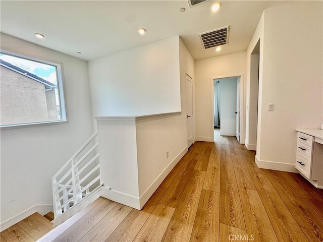 hallway featuring baseboards, visible vents, and light wood finished floors