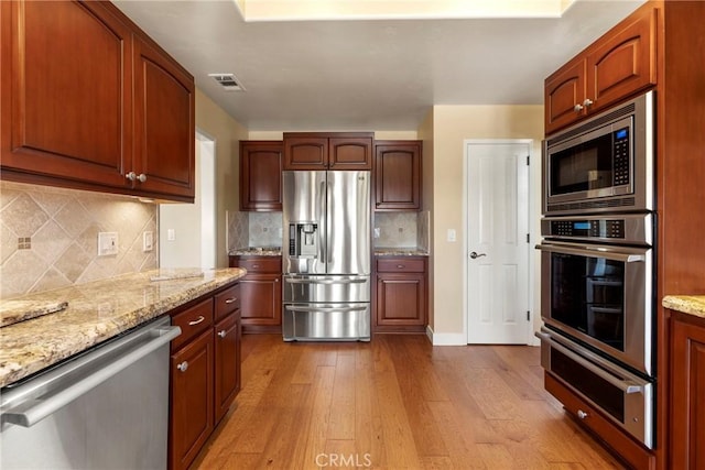 kitchen featuring visible vents, appliances with stainless steel finishes, wood finished floors, light stone counters, and a warming drawer