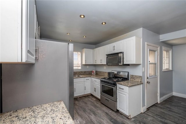 kitchen with light stone countertops, baseboards, dark wood-type flooring, white cabinetry, and stainless steel appliances
