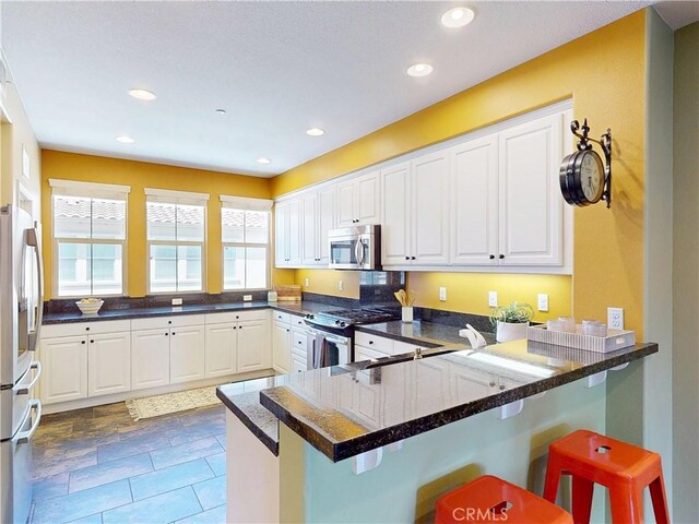 kitchen featuring white cabinets, stainless steel appliances, a kitchen bar, and a peninsula