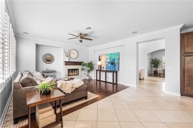 living area with crown molding, arched walkways, ceiling fan, light tile patterned floors, and a fireplace