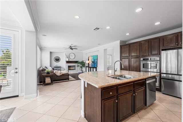 kitchen with appliances with stainless steel finishes, a sink, crown molding, a lit fireplace, and light tile patterned floors