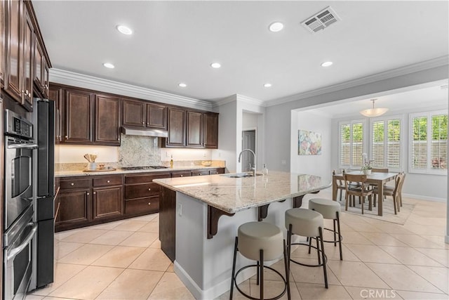 kitchen featuring a sink, under cabinet range hood, light tile patterned floors, a kitchen breakfast bar, and ornamental molding