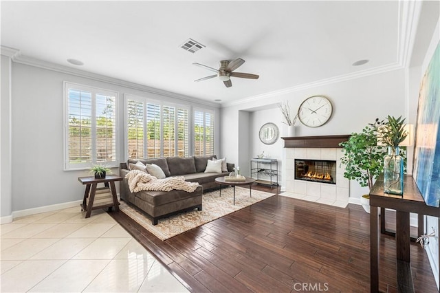 living area featuring crown molding, a ceiling fan, baseboards, a fireplace, and light wood-type flooring