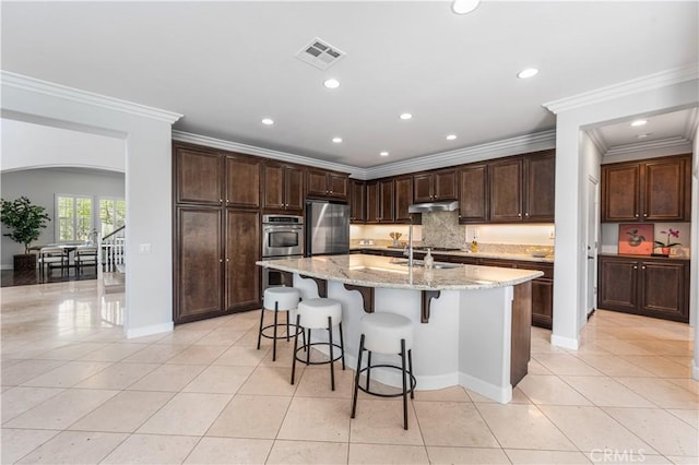 kitchen with stainless steel appliances, arched walkways, under cabinet range hood, light tile patterned floors, and crown molding