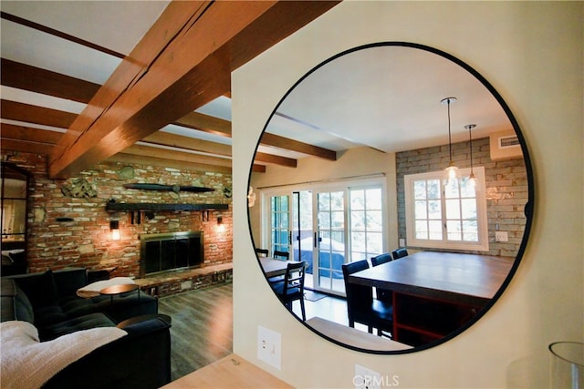 living room featuring brick wall, a brick fireplace, beam ceiling, and wood finished floors