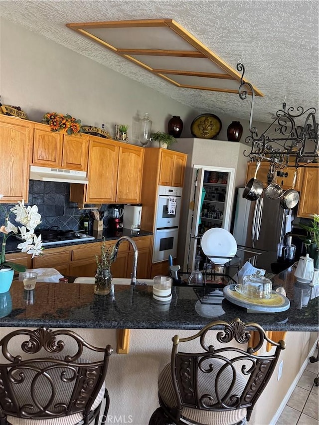 17815 Chestnut St, Hesperia, CA 92345 - kitchen with a textured ceiling, under cabinet range hood, gas cooktop, light tile patterned floors, and decorative backsplash