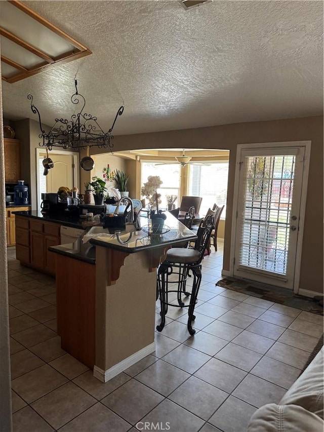 17815 Chestnut St, Hesperia, CA 92345 - kitchen with a textured ceiling, dark countertops, a breakfast bar area, light tile patterned floors, and a center island