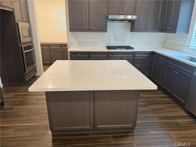 kitchen with a kitchen island, wood tiled floor, light countertops, under cabinet range hood, and stainless steel appliances