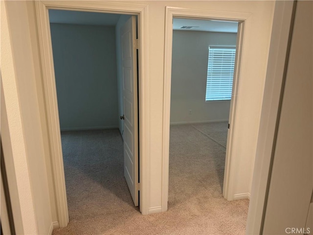 hallway with light colored carpet, baseboards, and visible vents