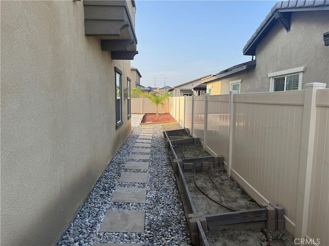 view of side of home with fence private yard, stucco siding, and a garden