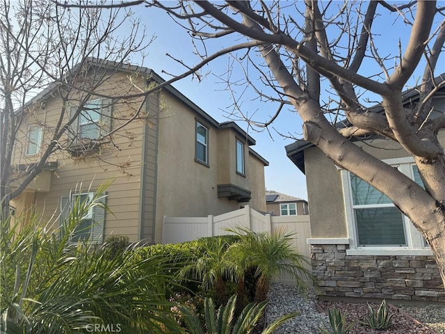 view of side of home with stucco siding, fence, and stone siding