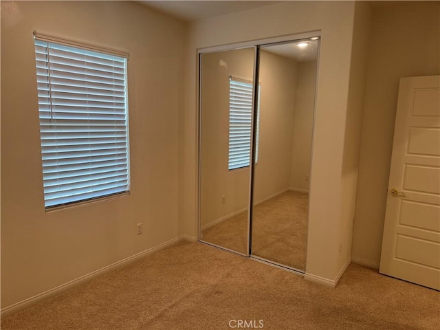 unfurnished bedroom featuring a closet, baseboards, multiple windows, and carpet flooring