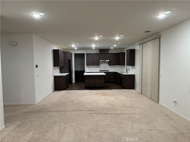 kitchen featuring a kitchen island, a sink, carpet floors, baseboards, and under cabinet range hood