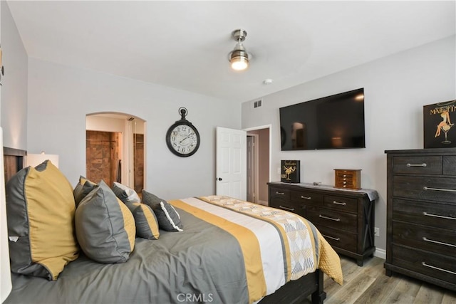 bedroom featuring arched walkways, visible vents, and light wood-style flooring