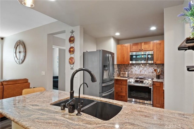 kitchen with decorative backsplash, appliances with stainless steel finishes, light stone countertops, a sink, and recessed lighting
