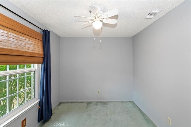 empty room featuring ceiling fan, a textured ceiling, light colored carpet, visible vents, and baseboards